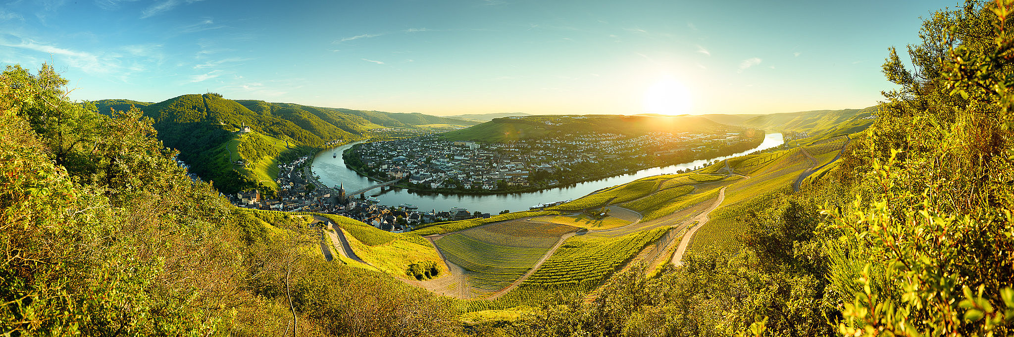 Moselpanorama mit Blick auf Bernkastel-Kues Moselpanorma mit Blick auf die Weinberge, die Mosel und die Stadt in Bernkastel-Kues im Abendlicht.