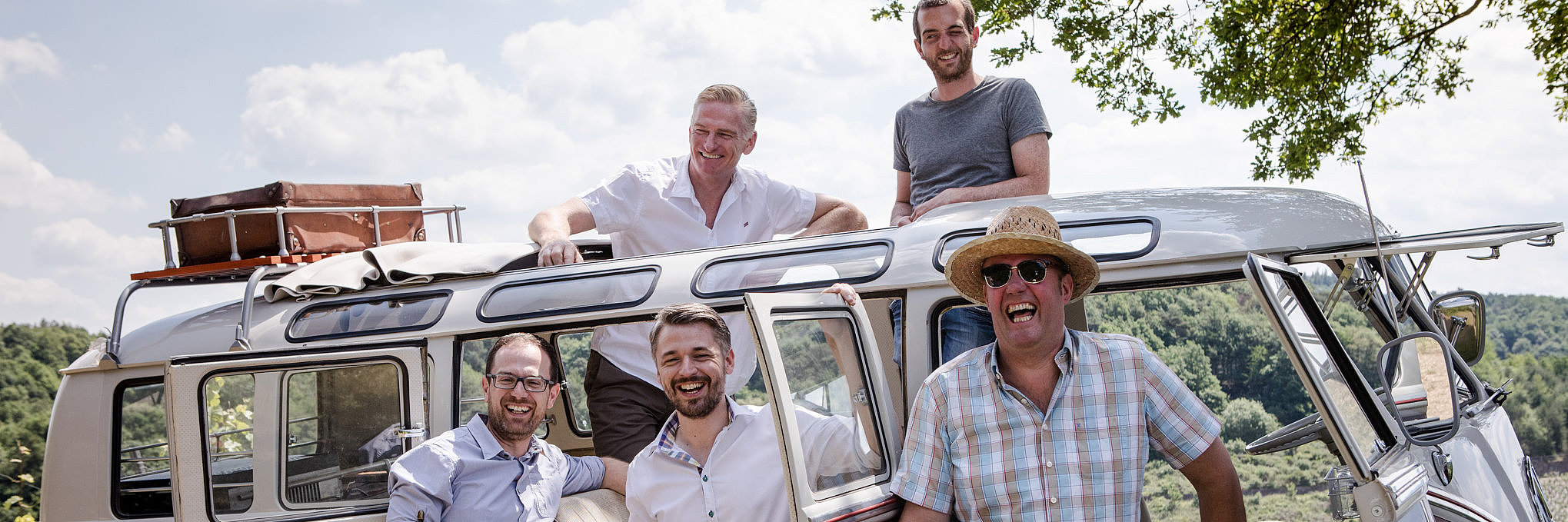Gesellige Bus-Tour durch die Weinberge an der Mosel Das Bild zeigt einen nostalgischen Bus mit geöffneten Türen. Darin und davor befinden sich insgesamt fünf Personen.