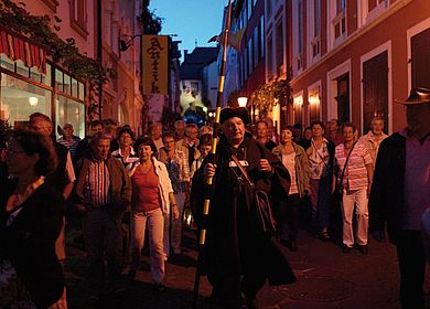 Freitzeitmöglichkeiten im Urlaub an der Mosel: Die Erlebnisführung Nachtwächtertour durch die Gassen der Altstadt von Bernkastel-Kues. Zu sehen ist der Gästeführer, der als Nachtwächter die Gäste durch die Stadt führt. 
