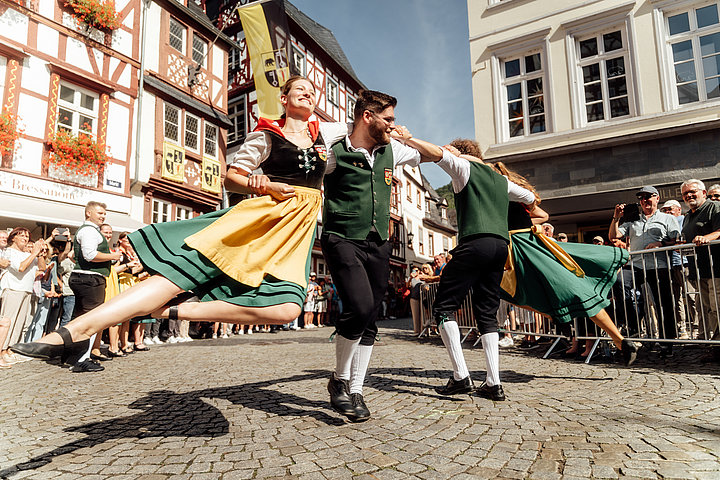 Eine traditionelle Winzertanzgruppe führt eine Figur auf, bei der zwei Frauen von zwei Männern in der Mitte im Kreis herumgewirbelt werden. Sie stehen dabei auf dem Marktplatz in Bernkastel-Kues anlässlich des Weinfestes der Mittelmosel.