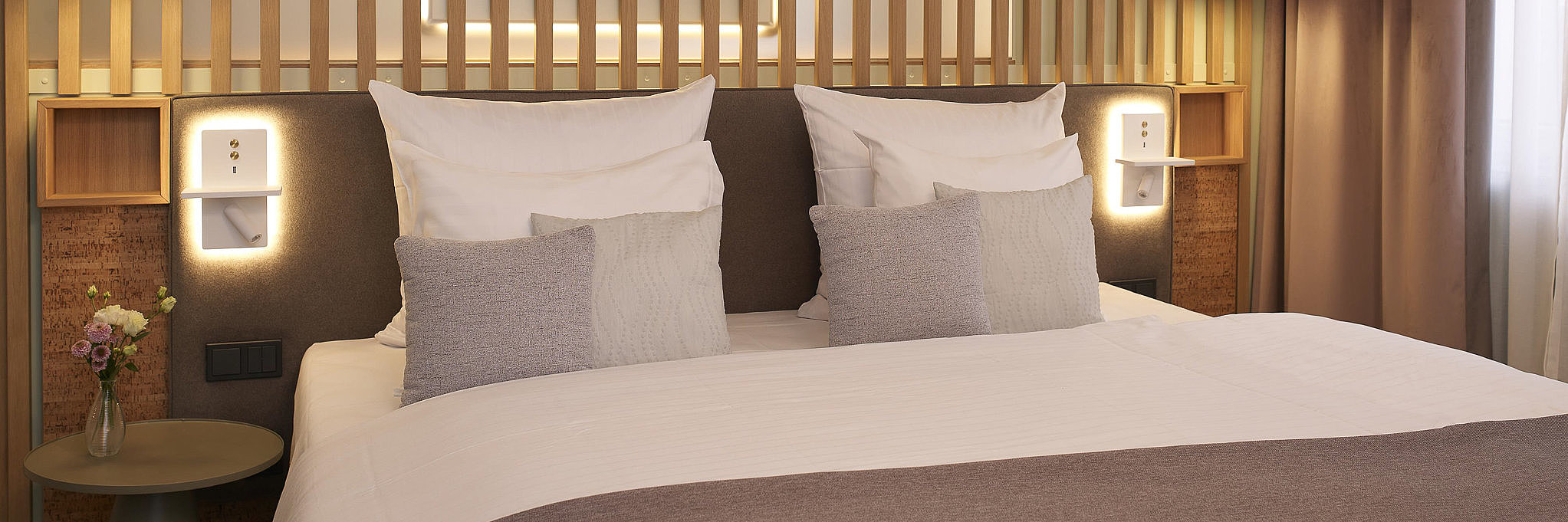 Das Bild zeigt ein modernes Hotelzimmer mit gemachtem Doppelbett.