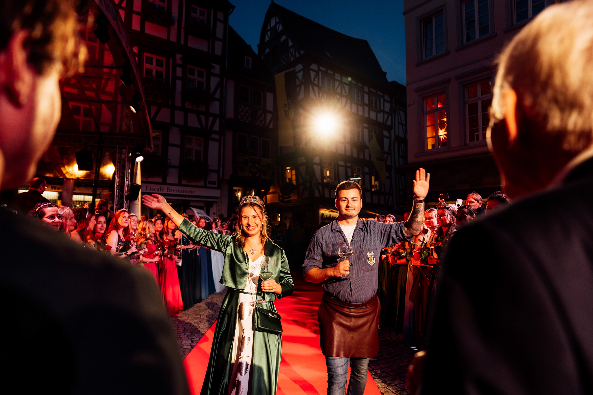 Eine Weinhoheit und ein im Winzerkittel gekleideter Mann laufen über einen roten Teppich und werden in Empfang genommen anlässlich des Weinfestes der Mittelmosel in Bernkastel-Kues.