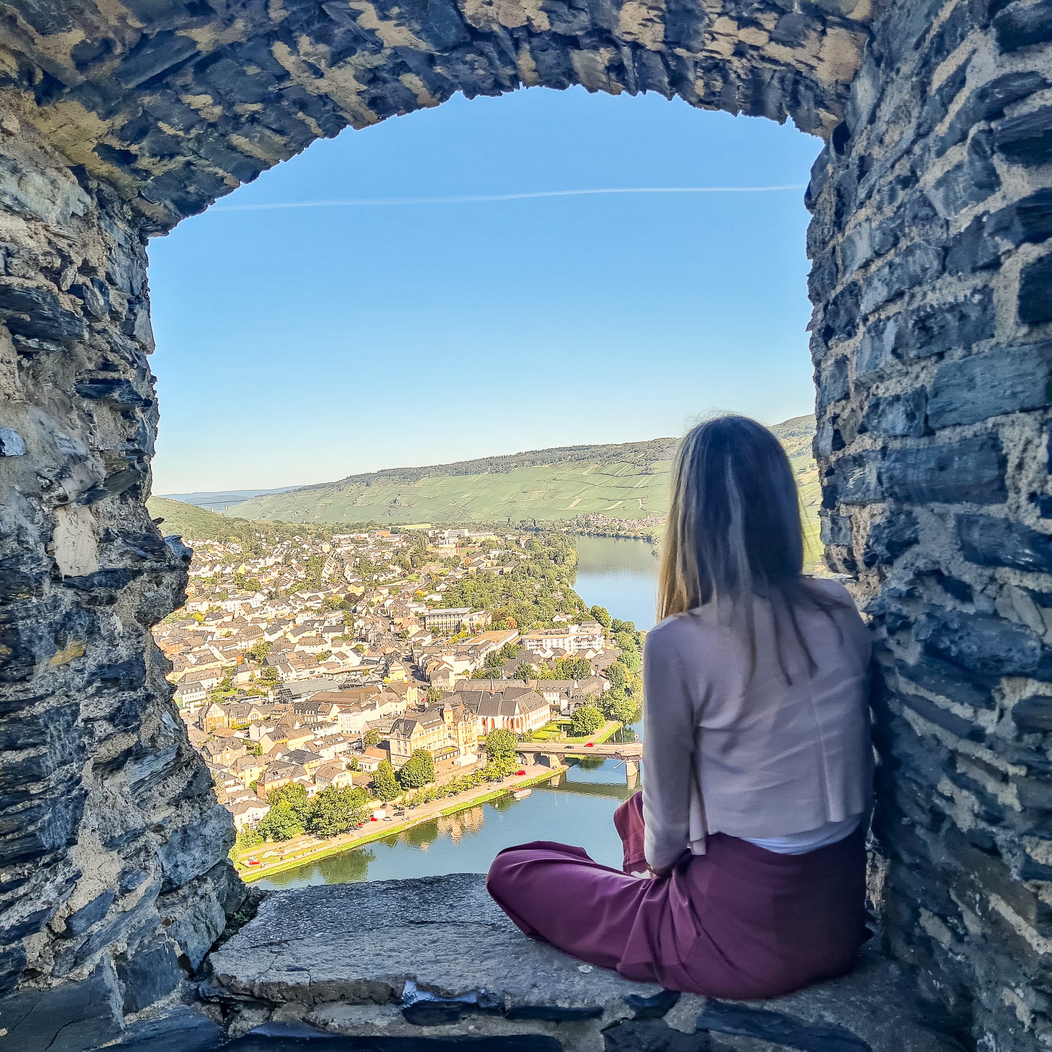 Person blickt von der Burg Landshut aus ins Moseltal Das Foto zeigt eine Person, die an einem Fenster sitzt und ins Moseltal schaut. Es handelt sich um einen historischen Gebäudeteil der ehemaligen Burg Landshut. Die Person blickt auf die Stadt Bernkastel-Kues.